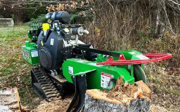 Grön stubbfräs med larvfötter redo att ta bort en stubbe i skogen.
