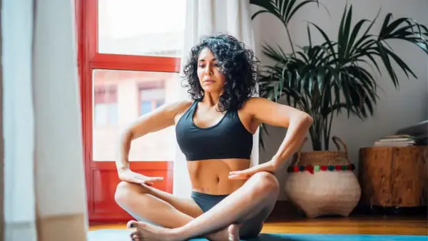 Mujer practicando hipopresivos postparto en casa, sentada en el suelo con las piernas cruzadas.