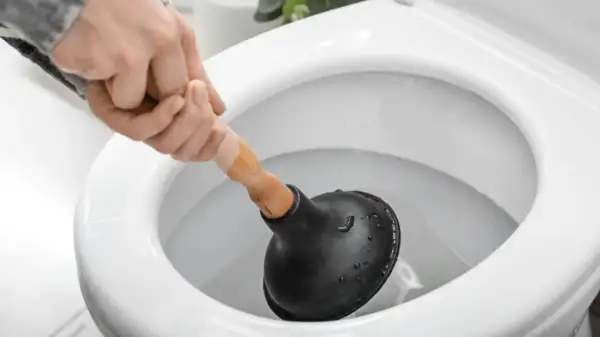 Main d'une personne utilisant une ventouse pour déboucher un WC.