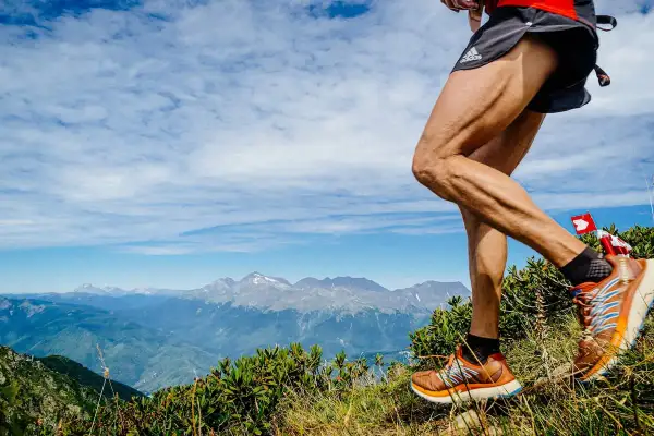 Un coureur en pleine descente trail sur un sentier de montagne, avec des sommets enneigés en arrière-plan.