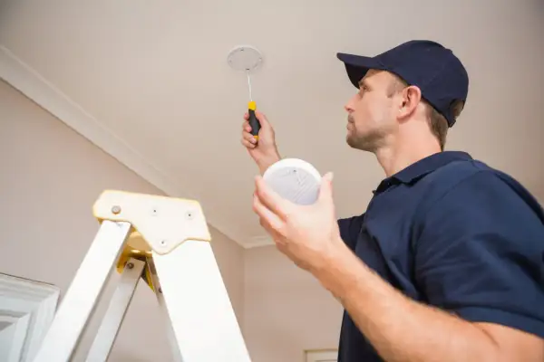 Un technicien installe des alarmes incendie au plafond, assurant la sécurité de votre domicile.
