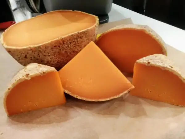Un queso mimolette peligroso, con su corteza rústica y su vibrante interior anaranjado, se presenta en cuñas y una pieza entera, invitando a una degustación audaz.