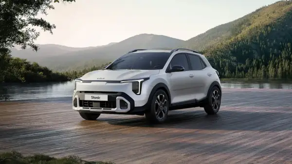Nowy Kia Stonic 2024, biały SUV, zaparkowany na drewnianym pomoście nad jeziorem, w otoczeniu gór i lasów.