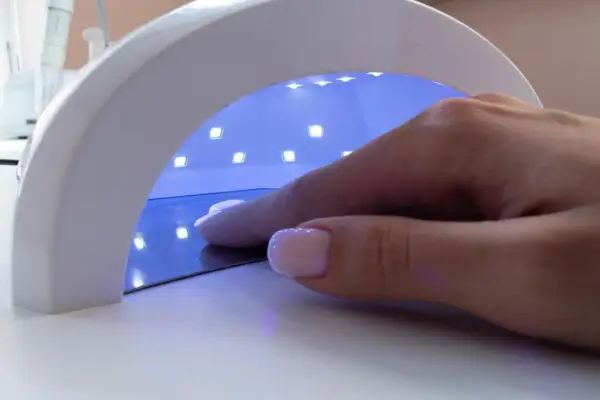 Dłoń z paznokciami w lampie UV. Zastanawiasz się, jaka moc lampy do paznokci będzie najlepsza?
