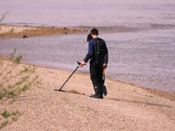 Mężczyzna z wykrywaczem metali i łopatką na plaży przy wodzie.