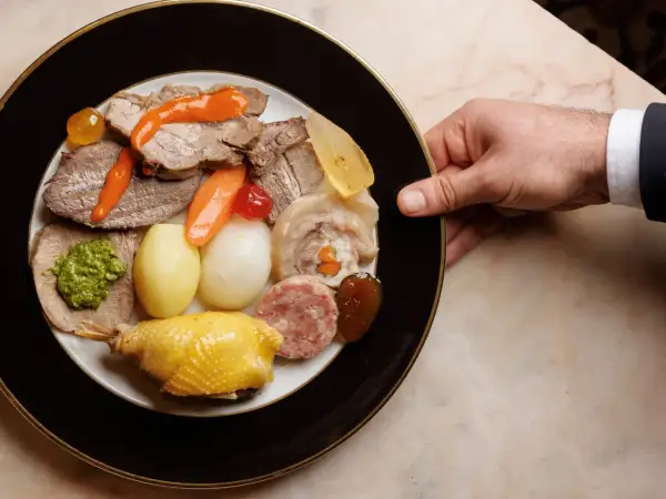 Un piatto ricco di bollito di carne, con verdure, salumi e un pollo arrosto, pronto per essere gustato.