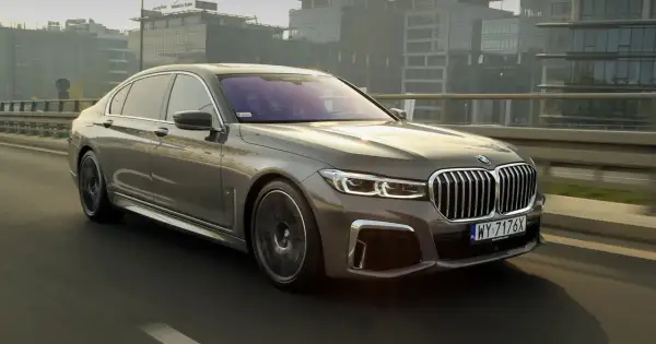 Eleganckie BMW 745Le w kolorze grafitowym sunie po moście, mijając nowoczesne budynki.