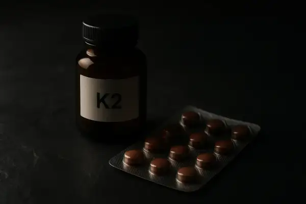Flacon étiqueté K2 et plaquette de comprimés bruns, rappelant l'importance de la vitamine K2 dans notre alimentation.