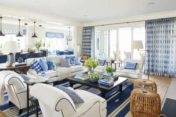 A bright living room with coastal interior design, featuring white sofas, blue and white patterned pillows, and a dark wood coffee table.
