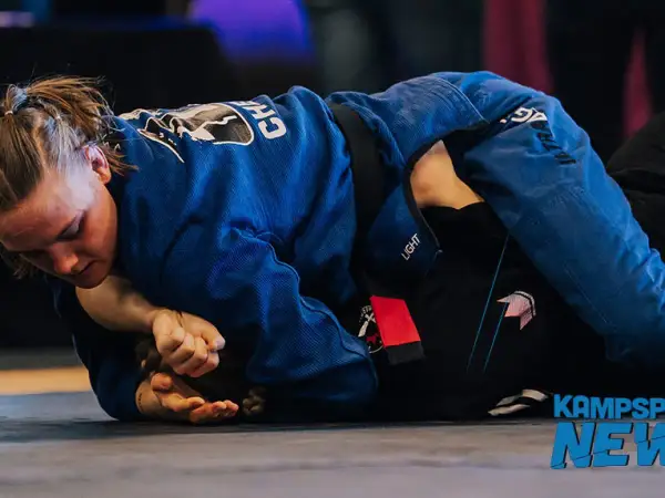 Två kvinnor i blå och svarta gi tävlar i bjj sm. En kämpar sig framåt, fokuserad på att vinna.