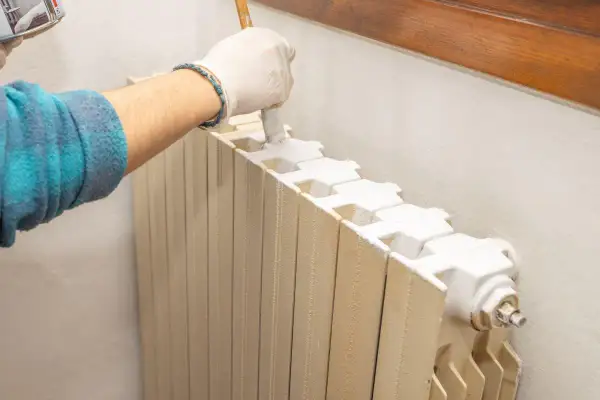 Mano con guanto bianco che dipinge un termosifone con pennello, un modo pratico per verniciare termosifoni senza smontarli.