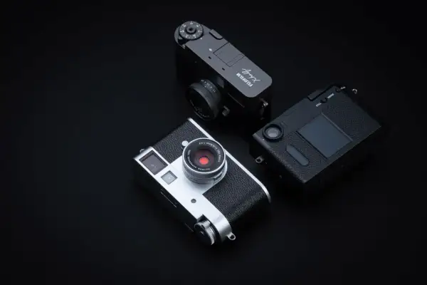 Tre fotocamere Fujifilm X-Half, una argento e due nere, disposte su sfondo scuro.