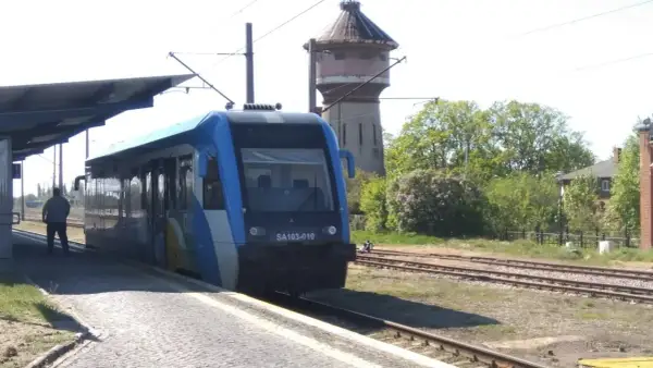 Niebieski pociąg SA103-010 czeka na pasażerów na peronie. W tle stara wieża ciśnień i drzewa. Wygodny wicie dojazd PKP.