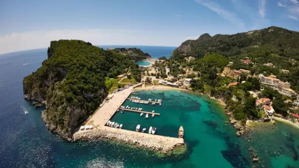 Malownicza zatoka na Korfu, idealna na wakacje z dzieckiem. Widać tu port z łodziami, plażę i zielone wzgórza.