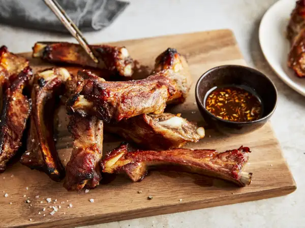 Saftige schweinerippchen braten, glasiert und mit Dip auf Holzbrett. Perfekt zum Genießen!