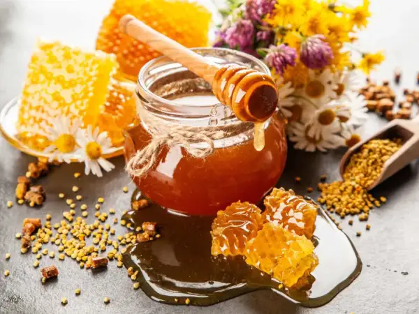 En burk gyllene honung, honungskaka och bipollen. Honung nyttigt för hälsan, omgiven av blommor.