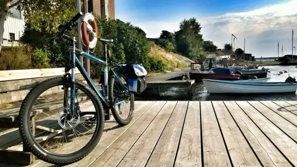 Rower z sakwami czeka na przygodę w Karlskronie. Drewniany pomost, łodzie i błękitne niebo zapraszają do odkrywania uroków wybrzeża.
