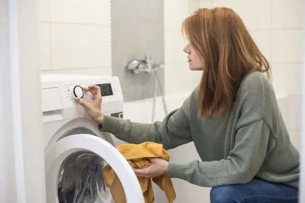 Donna con capelli rossi imposta la lavatrice. Ricorda che lavare a 30 gradi disinfetta, un modo semplice per prendersi cura dei tuoi capi.