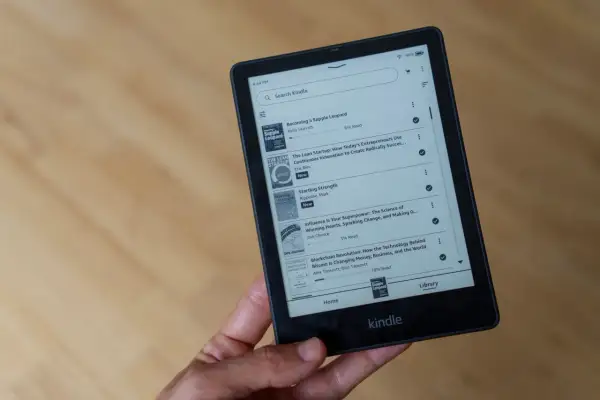 Main d'une personne tenant un livre format Kindle affichant une liste de titres, dont "Becoming a Supple Leopard" et "The Lean Startup".