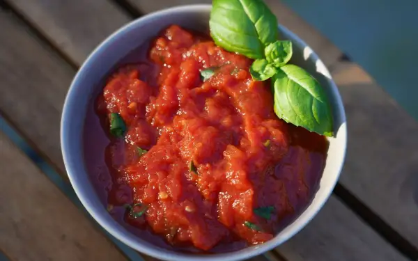 Schüssel mit frischer, stückiger Tomatensoße, wie in der Pizzeria, garniert mit Basilikum. Perfekt für hausgemachte Pizza.