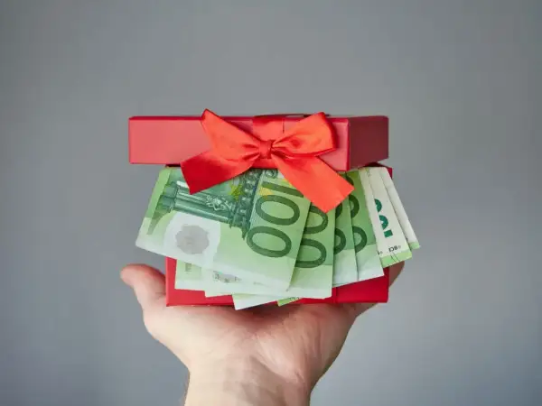 Czerwone pudełko z prezentem i banknotami euro na dłoni.