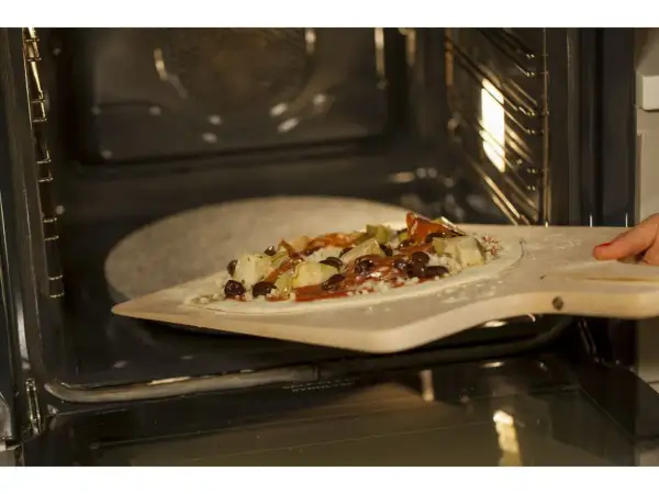 Pizza z dodatkami na łopacie do pizzy, gotowa do wsunięcia na kamień do pizzy granitowy w rozgrzanym piekarniku.