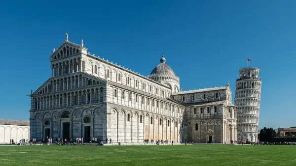 La piazza dei Miracoli a Pisa con il Duomo e la celebre torre di Pisa, simbolo della città, sotto un cielo azzurro.