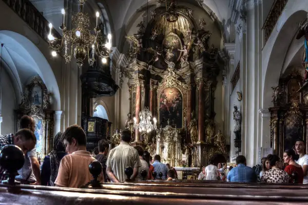 Ludzie uczestniczą w liturgii mszy świętej w bogato zdobionej, barokowej świątyni.