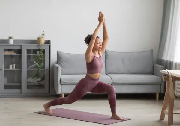 Femme pratiquant le yoga à la maison gratuit, en posture de guerrier, dans un salon moderne.