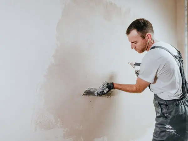 Operaio con spatola applica intonaco su muro. La rasatura è un passaggio cruciale per una finitura perfetta.