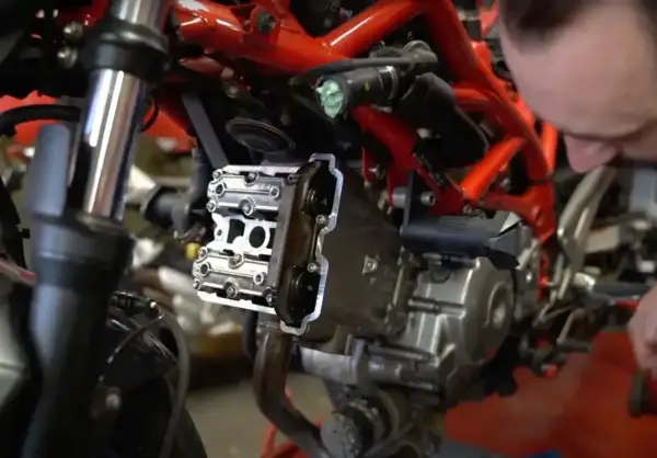 Mechanik pracuje nad silnikiem motocykla, pokazując, jak ustawić zawory.