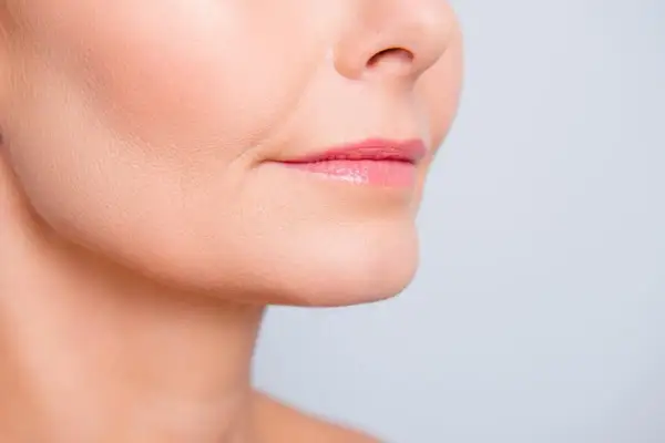 Primer plano de labios rosados y piel con un ligero surco nasogeniano, mostrando detalles de la textura facial.