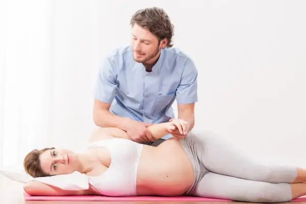 Fisioterapeuta ayuda a una mujer embarazada con un masaje perineal, preparándola para el parto.