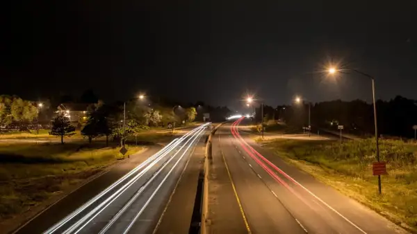 Luces de coches dejan estelas blancas y rojas en la carretera de noche, iluminada por el alumbrado de carretera.