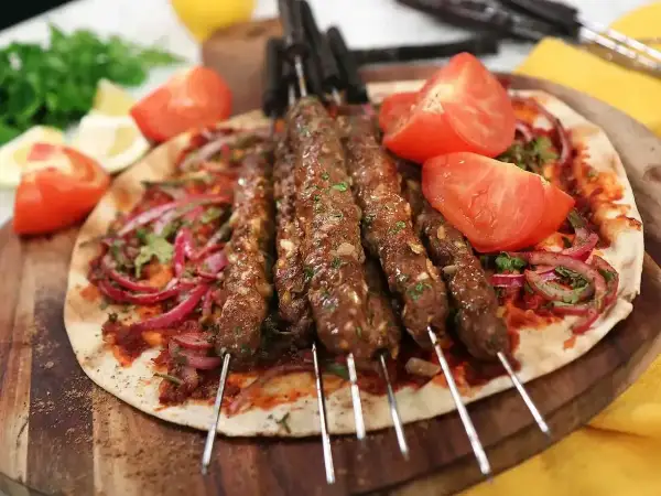 Grillad adana kebab på spett, serverad med tunnbröd, rödlök, tomat och persilja. Ett perfekt adana kebab recept för sommaren.