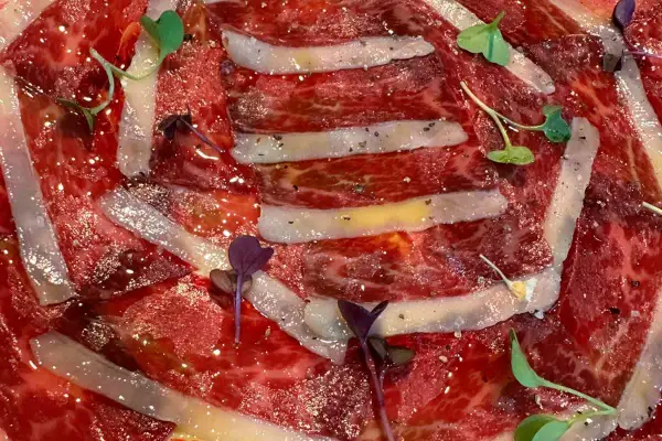Finas lonchas de jamón ibérico, un manjar de moda, con un toque de pimienta y brotes verdes.