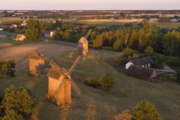 Wielkopolska atrakcje: drewniane wiatraki na tle zachodzącego słońca, malowniczy krajobraz wsi i pól.