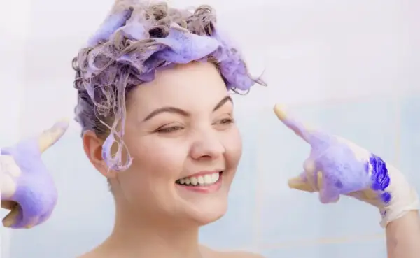 Sonrisa radiante con cabello teñido de violeta, lista para el antes y después. Guantes con espuma violeta.
