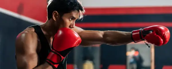 Boxer throws a powerful punch, aiming for the sternum. Red gloves flash as he trains in the ring.