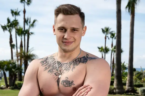 Daniel Majewski, młody mężczyzna z tatuażami na klatce piersiowej, pozuje na tle palm i błękitnego nieba.