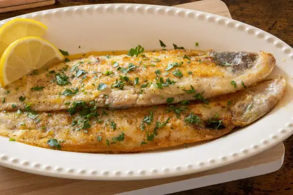 Delicioso lenguado a la plancha, dorado y jugoso, adornado con perejil fresco y rodajas de limón.