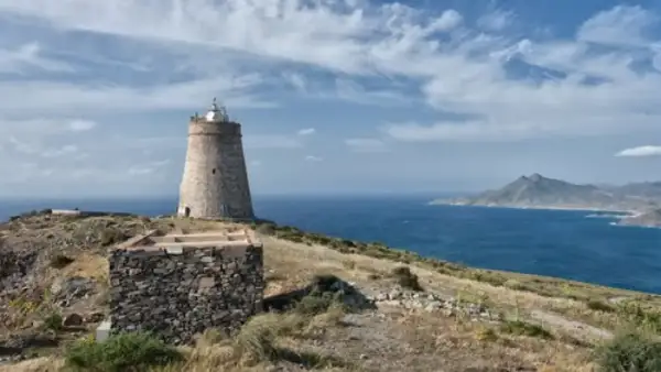 El faro de Almería se alza sobre una colina rocosa, vigilando el mar azul bajo un cielo nublado.