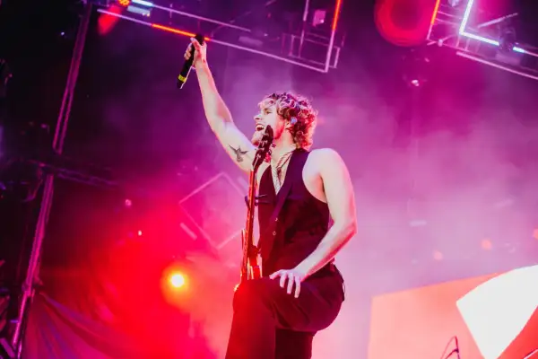 Luke Hemmings z 5 Seconds of Summer Polska na koncercie, z mikrofonem w dłoni i gitarą.