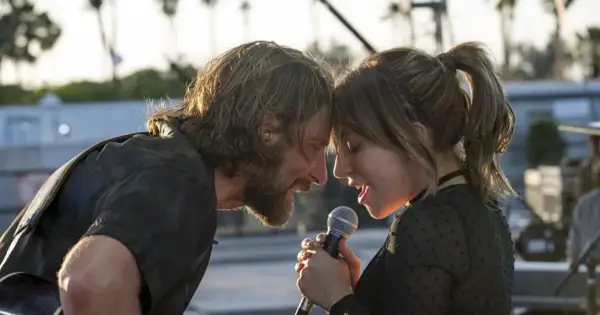Bradley Cooper i Lady Gaga śpiewają razem, zbliżając twarze do mikrofonu.