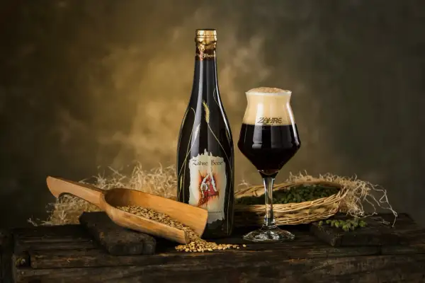 Una bottiglia e un bicchiere di birra Zahre, con chicchi d'orzo e luppolo, ingredienti per una birra artigianale di qualità.