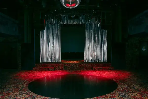 Scène de concert avec rideaux argentés, tapis persan et boule disco rougeoyante, évoquant l'ambiance d'un bus palladium.