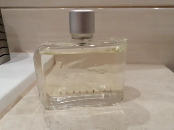 Szklana butelka perfum Lacoste Essential Sport z srebrną nakrętką, stojąca na blacie.