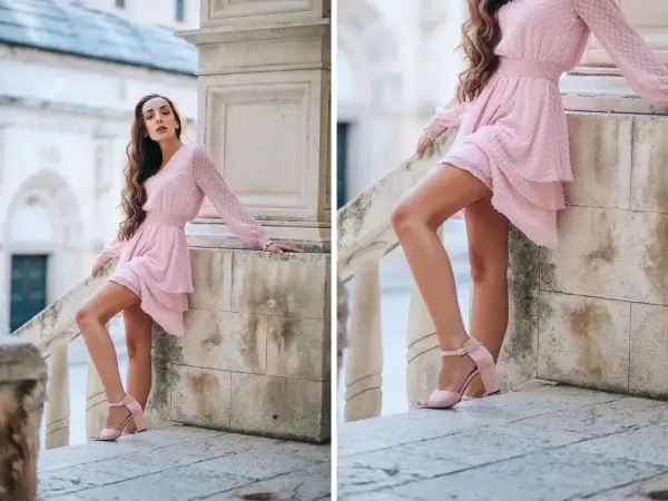Kobieta w pudrowej sukience i pasujących do niej sandałkach na obcasie. Idealne buty do pudrowej sukienki na letnie wyjście.