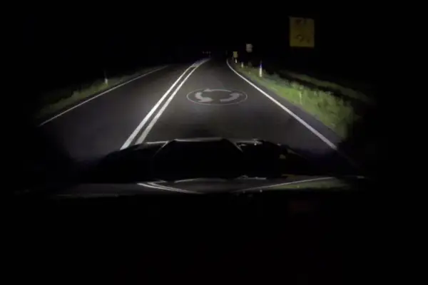 La route de nuit, éclairée par les feux de route, révèle un rond-point.