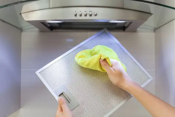 Hand reinigt mit gelbem Tuch den Metallfilter einer Dunstabzugshaube, um klebrige Rückstände zu entfernen.